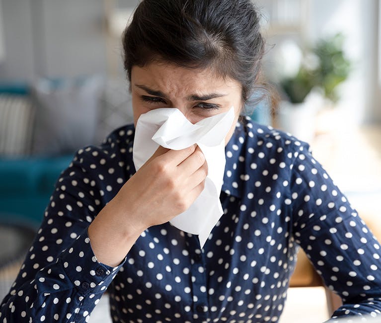 A black-haired woman is trying to blow her nose in a tissue