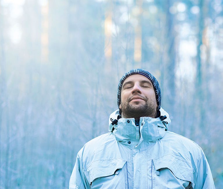 A man is wearing a warm hat and coat whilst breathing in the cool winter air.