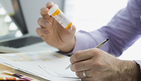 Doctor holding a pill bottle and writing a prescription Doctor holding a pill bottle and writing a prescription