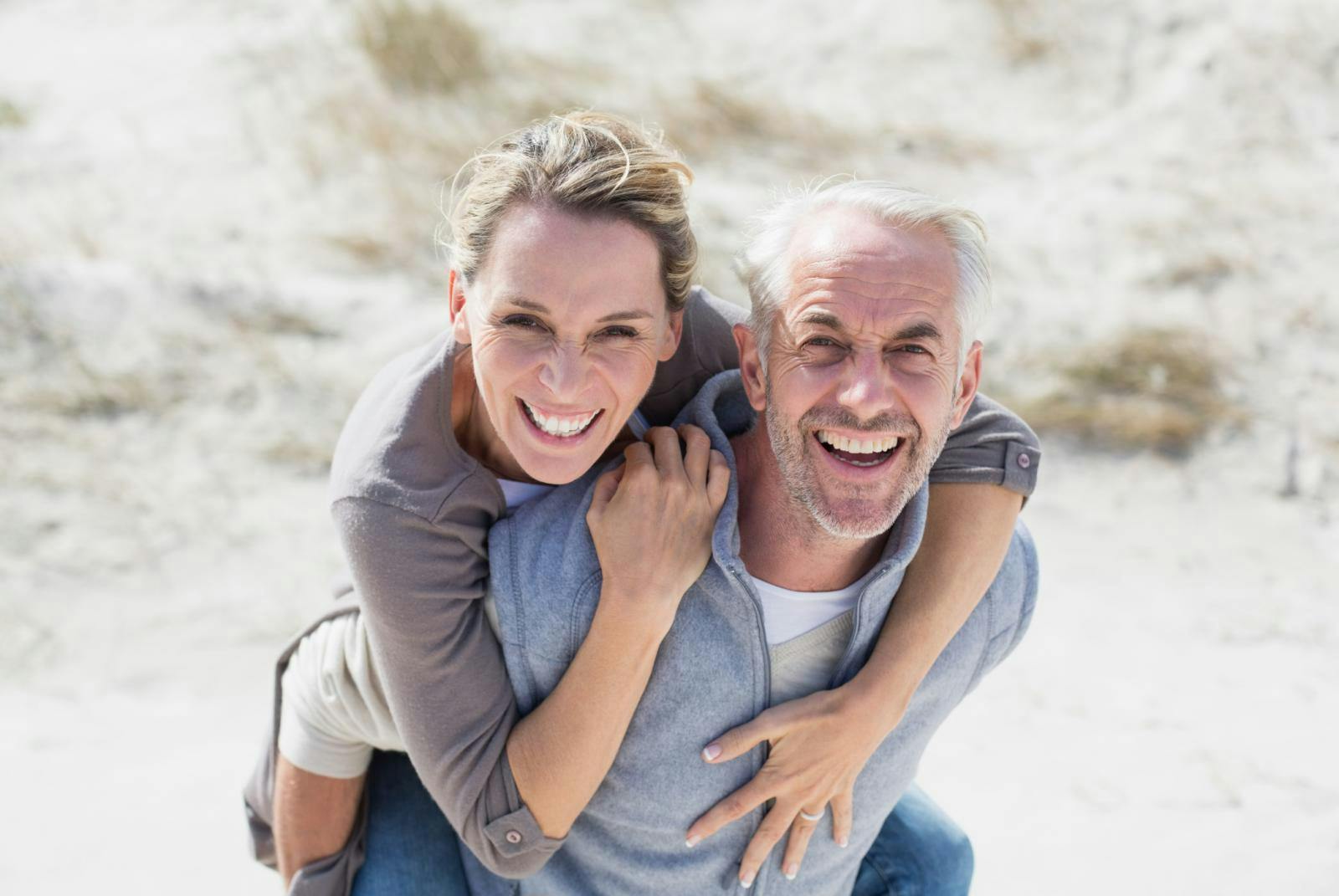 Elderly man giving a woman a piggyback ride on the beach. Elderly man giving a woman a piggyback ride on the beach.