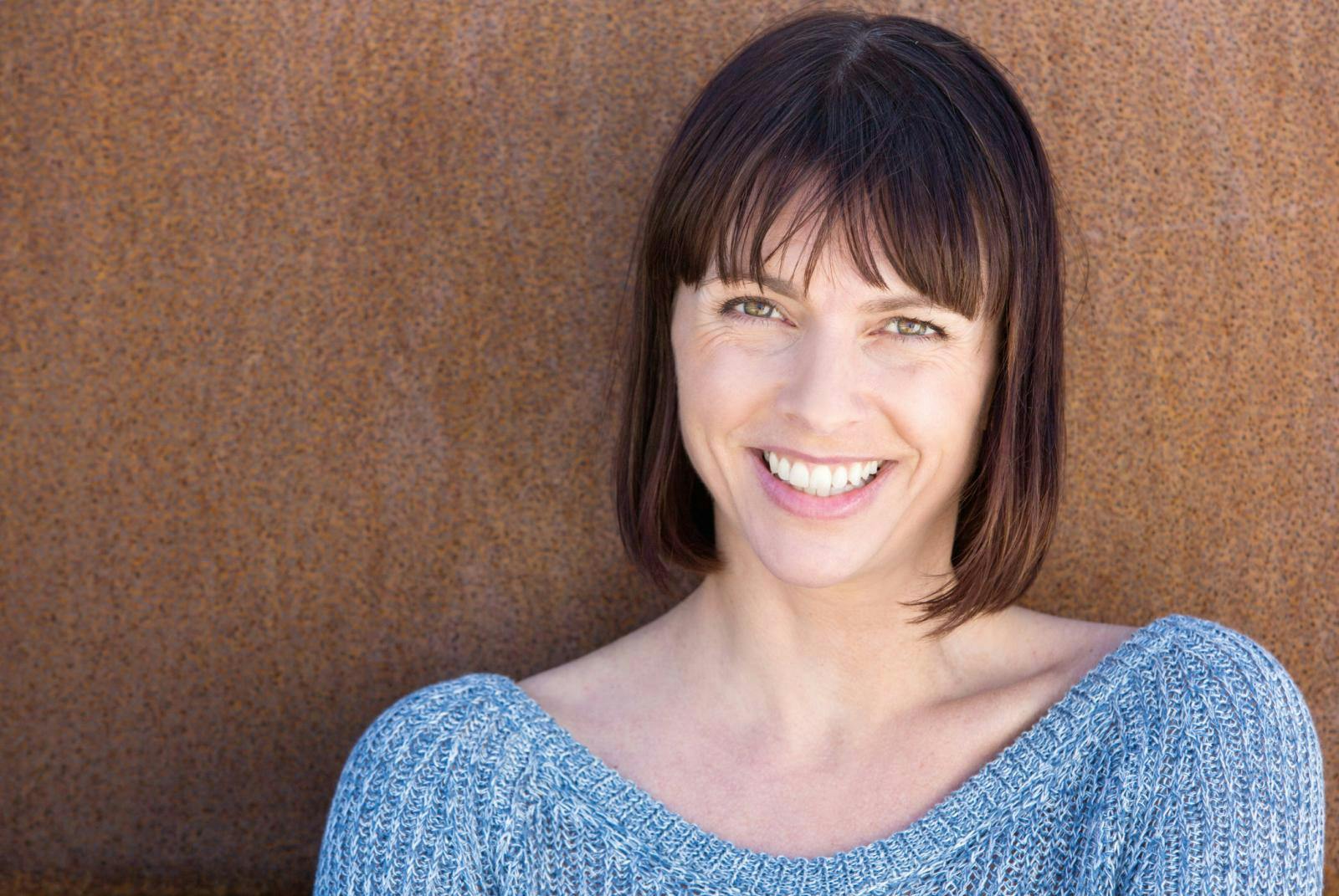 Smiling woman standing in front of a brown wall Smiling woman standing in front of a brown wall