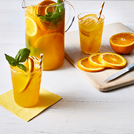 Pitcher and glasses filled with Orange Basil Sparkler drink beside slices of fresh orange Pitcher and glasses filled with Orange Basil Sparkler drink beside slices of fresh orange
