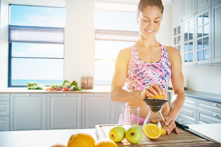 Smiling woman juicing oranges and other fruits in a bright kitchen