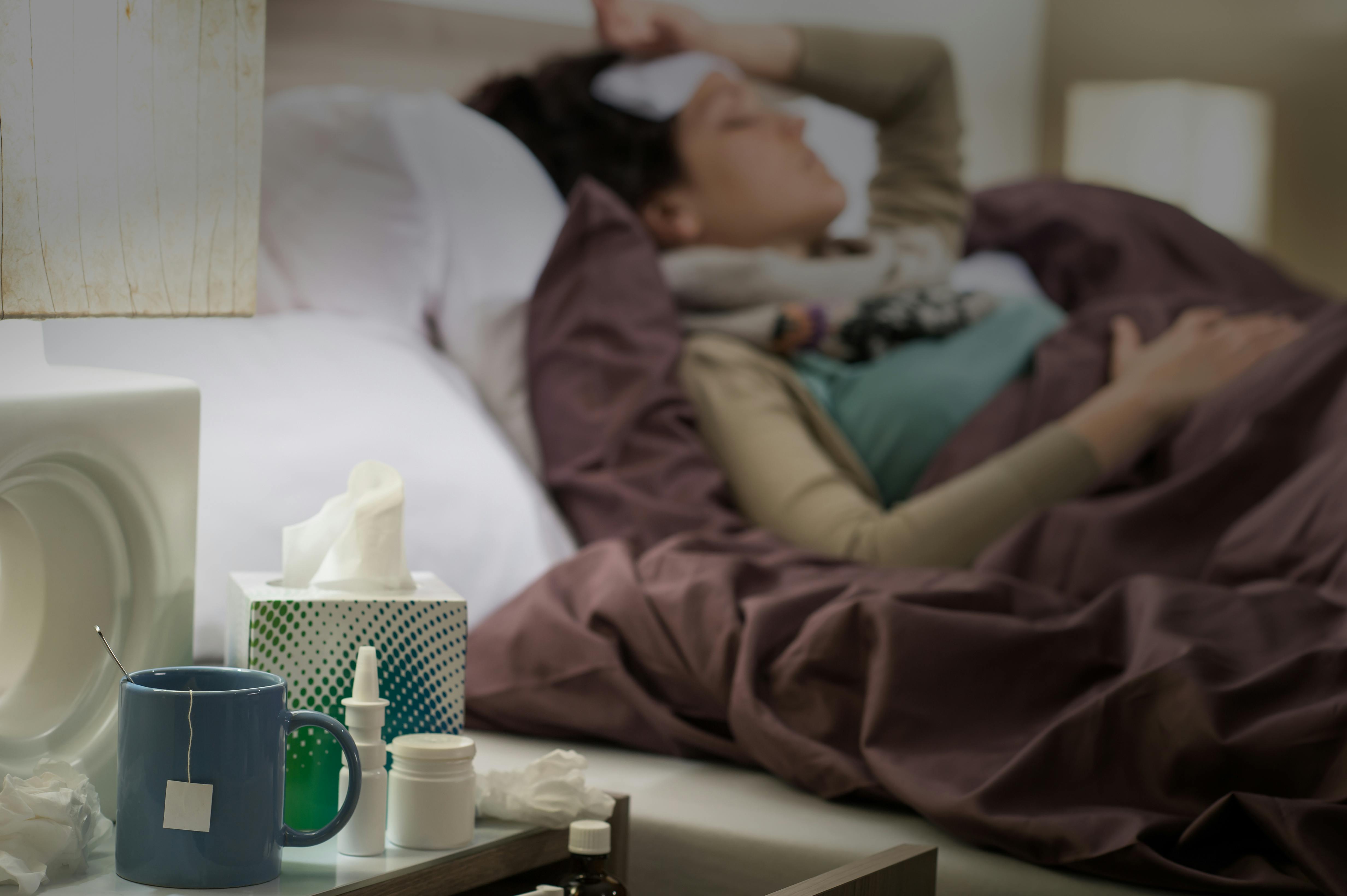 Woman lying in bed sick with flu medicines on the bedside table Woman lying in bed sick with flu medicines on the bedside table
