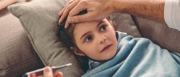 561769342 Sick child laying on couch while parent looks at a thermometer