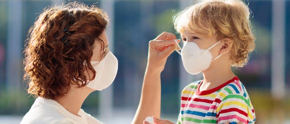 Mother helping child put on their face mask Mother helping child put on their face mask