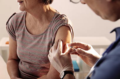 A woman is receiving a shot in her upper arm from a medical professional