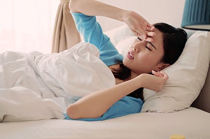 A woman lying in bed is holding her hand to her head