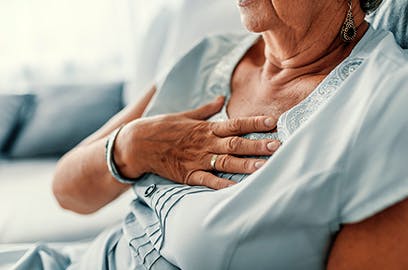 A woman is sitting down with her hand to her chest