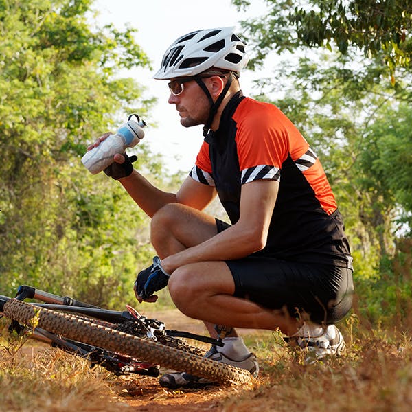Man drinking water while crouching near bicycle Man drinking water while crouching near bicycle