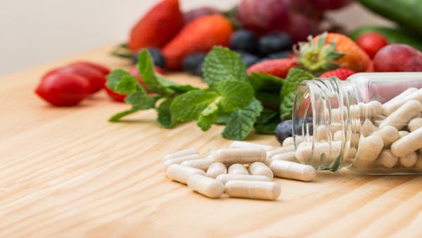 glass jar with capsules on its side with the capsules spilling out in front of cherry tomatoes, grapes, strawberries, and blueberries glass jar with capsules on its side with the capsules spilling out in front of cherry tomatoes, grapes, strawberries, and blueberries