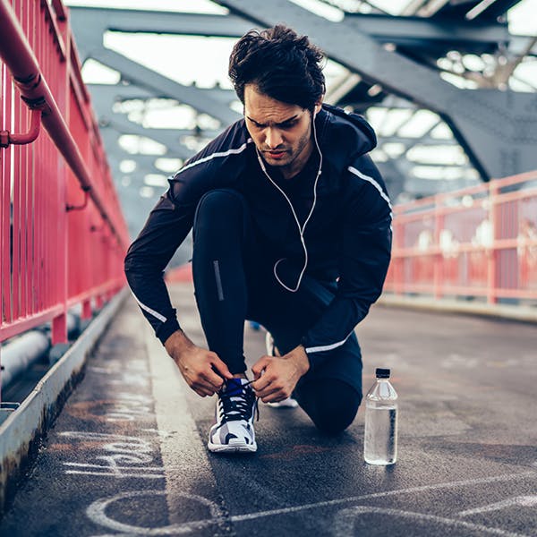 Man kneeling to tie his shoes while outside on a run Man kneeling to tie his shoes while outside on a run