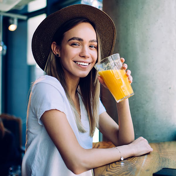 Smiling woman with a hat on drinking an orange drink Smiling woman with a hat on drinking an orange drink
