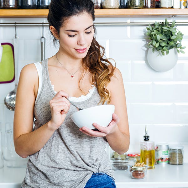 Woman eating a bowl of food in her kitchen Woman eating a bowl of food in her kitchen