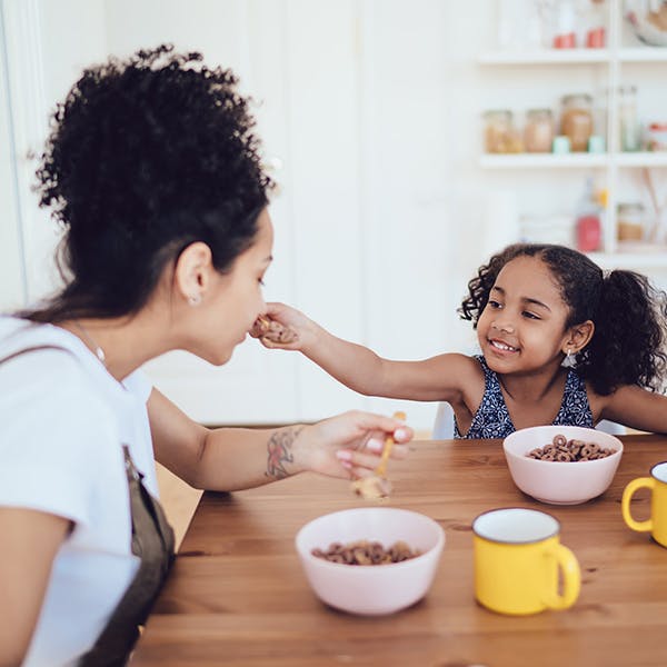 Woman and her daughter eating breakfast cereal together Woman and her daughter eating breakfast cereal together