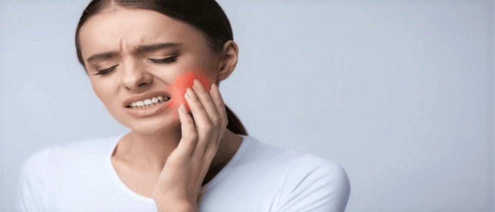 Women holding the side of her cheek by her jaw inpain