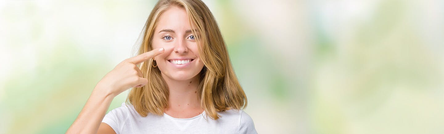 Young woman points to her nose, an organ of the respiratory system that helps you breathe by filtering impurities from the air.
