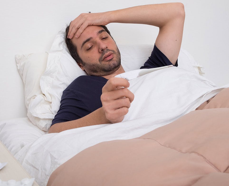 A man in bed reading an article about fever remedies A man in bed reading an article about fever remedies