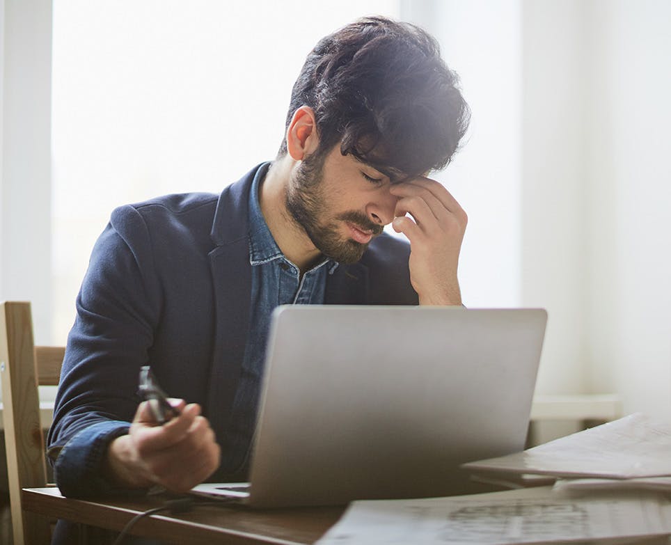 A man working on his computer while dealing with a migraine A man working on his computer while dealing with a migraine