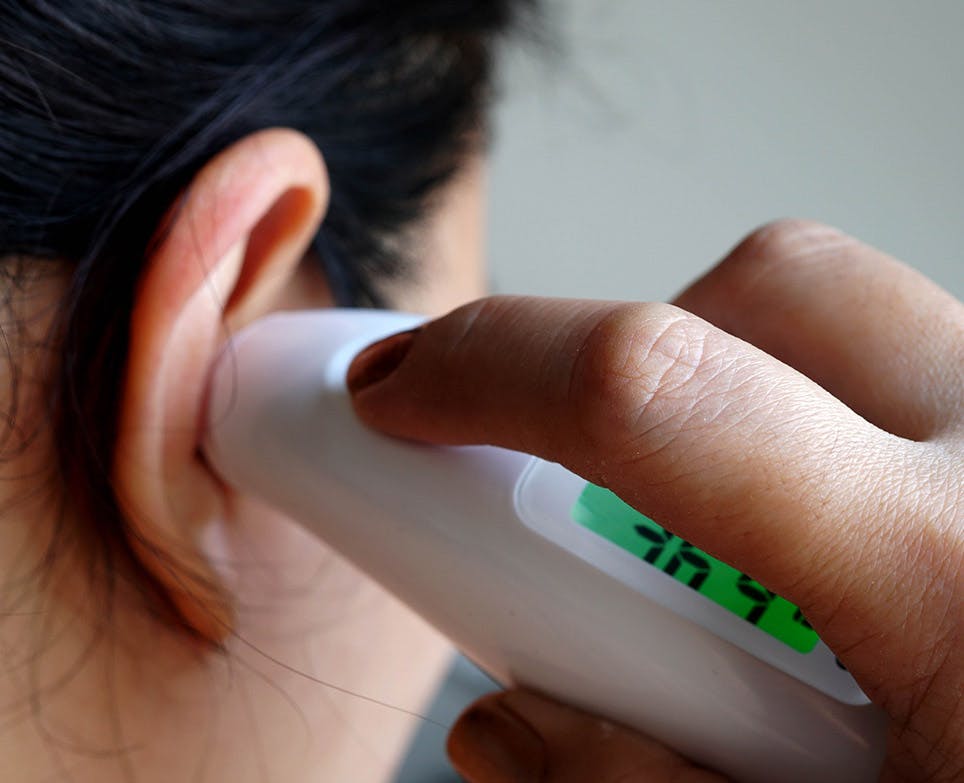 Person taking their temperature with a digital ear thermometer. Person taking their temperature with a digital ear thermometer.