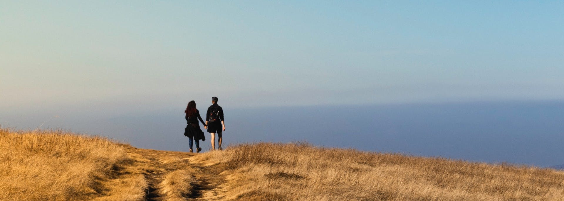 Boy and girl holding hands walking on yellow grassy plain with clear blue skies