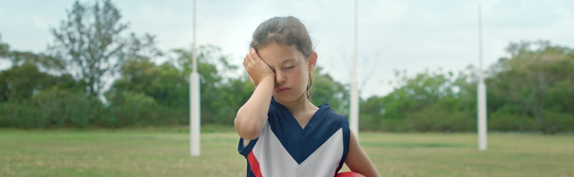 Kid in sports clothes rubbing their eye
