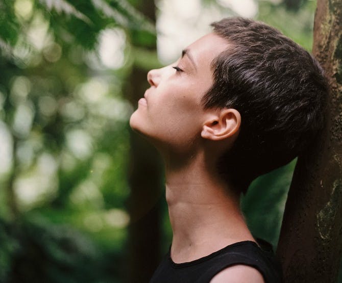 Person leaning against tree peacefully with her eyes closed