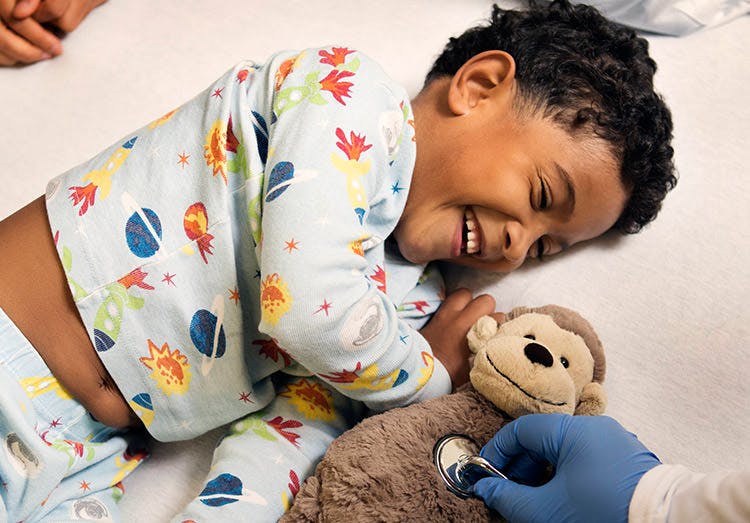Dreng ligger med sin bamse og ler
