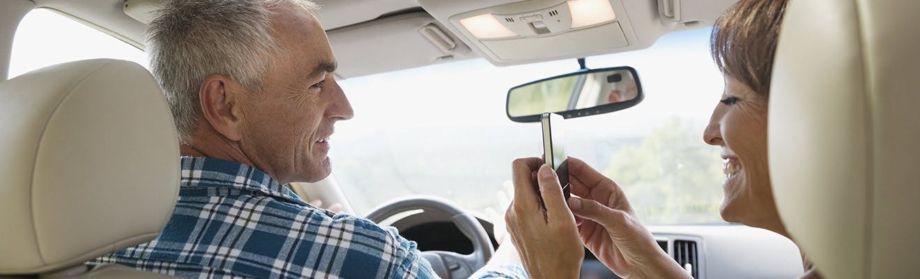 Older couple in a car and taking a picture of mans smile with dentures Older couple in a car and taking a picture of mans smile with dentures