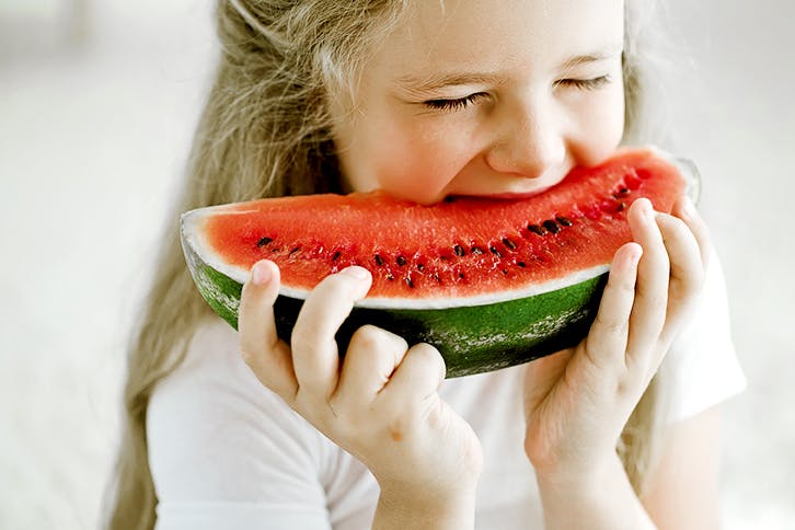 Petite fille en train de mordre dans une tranche de melon d'eau Petite fille en train de mordre dans une tranche de melon d'eau