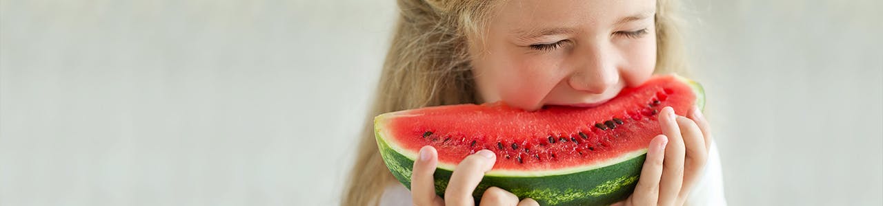 Petite fille en train de mordre dans une tranche de melon d'eau Petite fille en train de mordre dans une tranche de melon d'eau