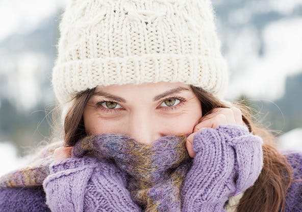 Woman wearing a white winter hat and covering her face with a purple scarf Woman wearing a white winter hat and covering her face with a purple scarf