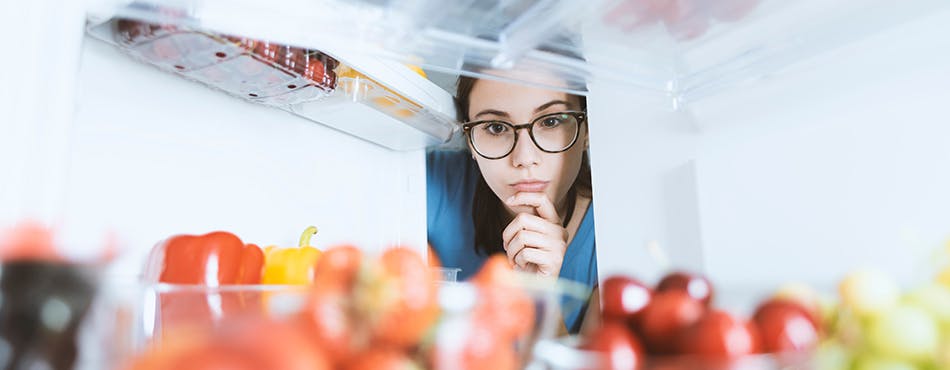 Young woman looking intently at fresh food in fridge Young woman looking intently at fresh food in fridge