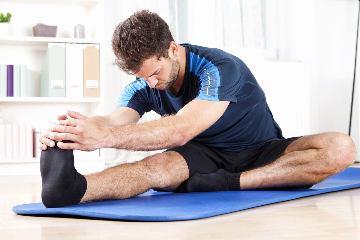 Man in his mid-thirties doing hamstring stretches on a blue yoga mat
